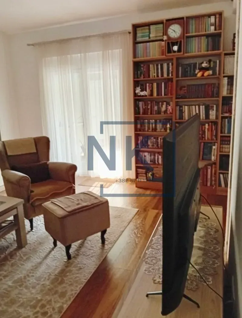 Dnevna soba sa foteljom, policom za knjige i televizorom.
