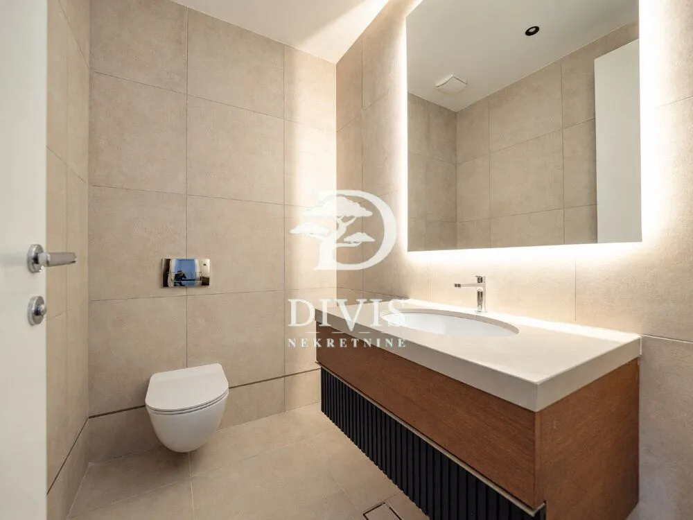 Modern bathroom equipped with a washbasin, wall-hung toilet, and a large backlit mirror.
