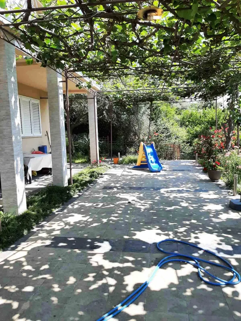 Popločano dvorište u hladovini vinove loze sa dječjim toboganom.