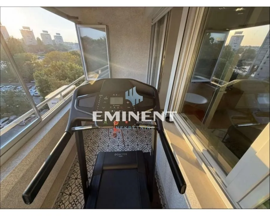 Enclosed balcony with a treadmill and city view.