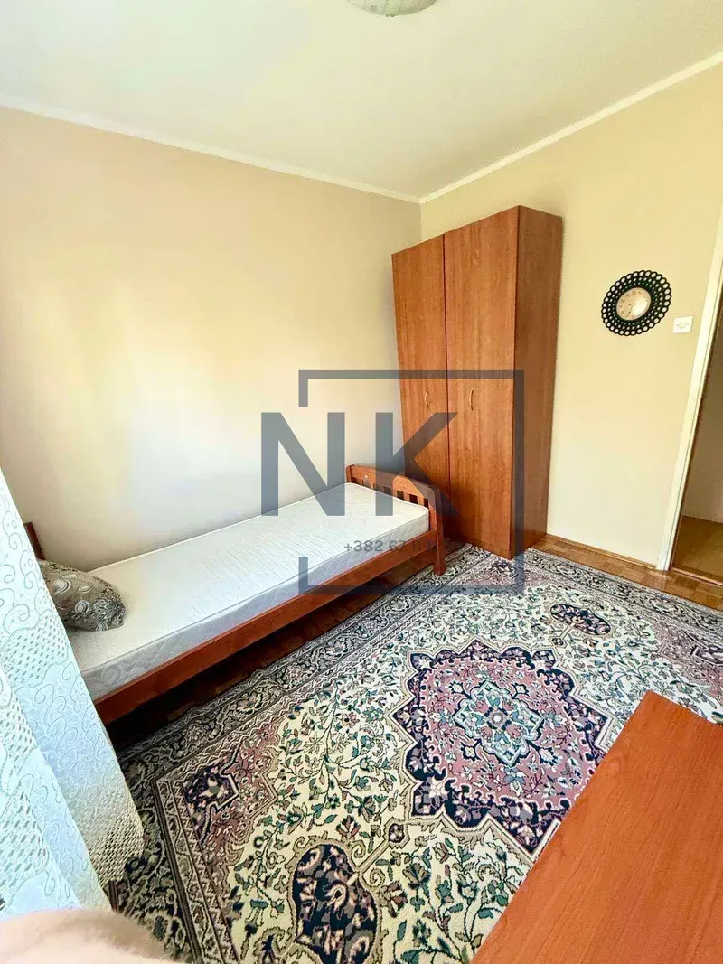 Small bedroom with a bed, wooden wardrobe, and a rug.