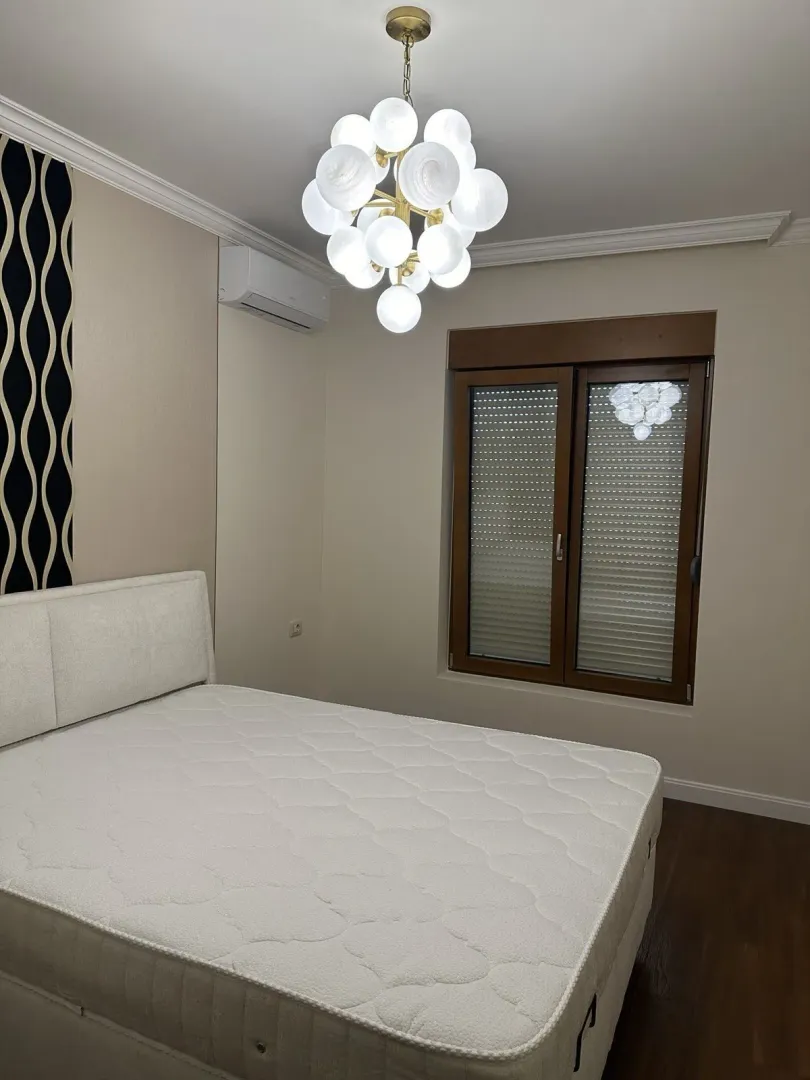 Svijetla spavaća soba sa velikim krevetom i modernim lusterom.