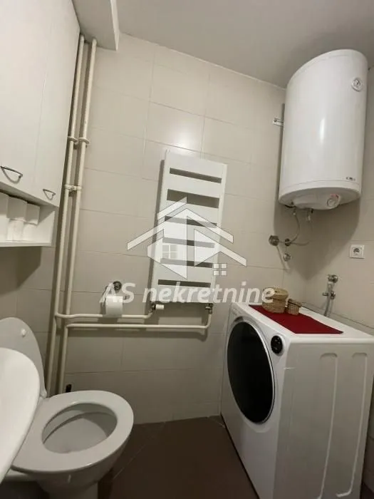Manje kupatilo sa WC šoljom, veš mašinom i bojlerom.