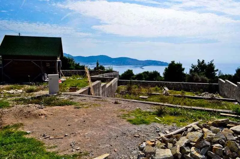 Pogled na plac sa manjom drvenom kućom i pogledom na more u pozadini.