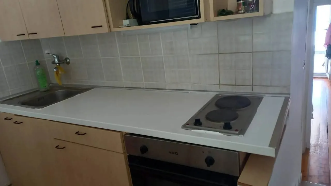 Manja kuhinja sa sudoperom, ugradnom pločom i elementima od drveta.