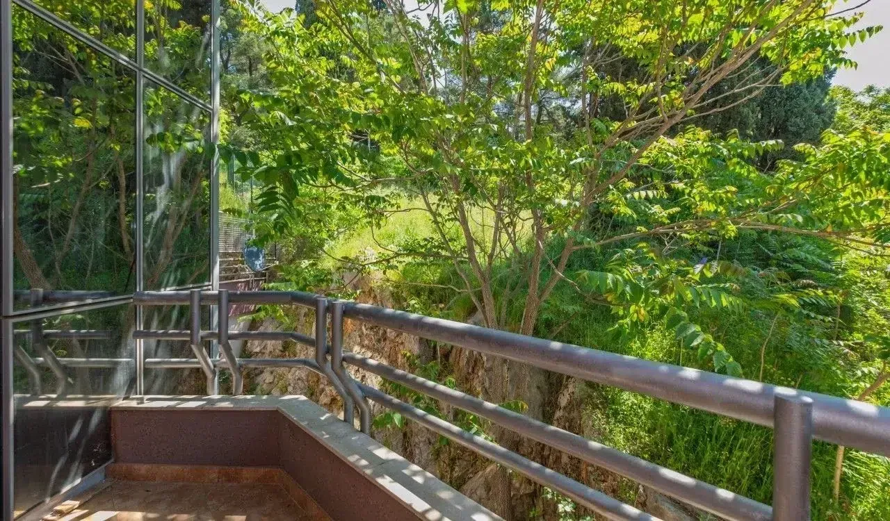 Balkon sa metalnom ogradom i pogledom na zeleno okruženje.