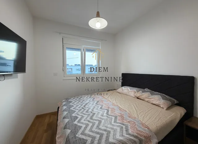 Namještena spavaća soba sa bračnim krevetom, prozorom i televizorom na zidu.