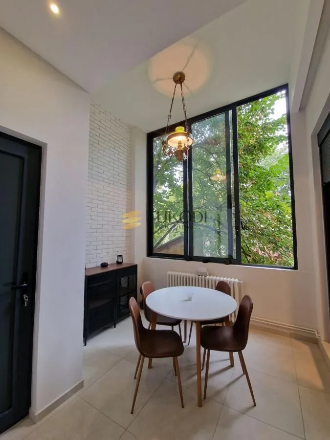 Dining area with a round table, four chairs and a large window overlooking greenery.