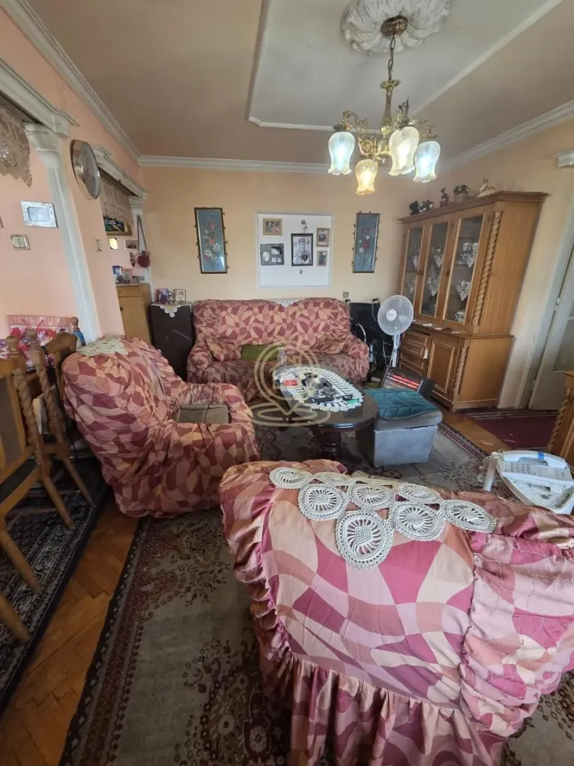 Dnevna soba sa garniturom za sedenje, drvenim nameštajem i lusterom na plafonu.
