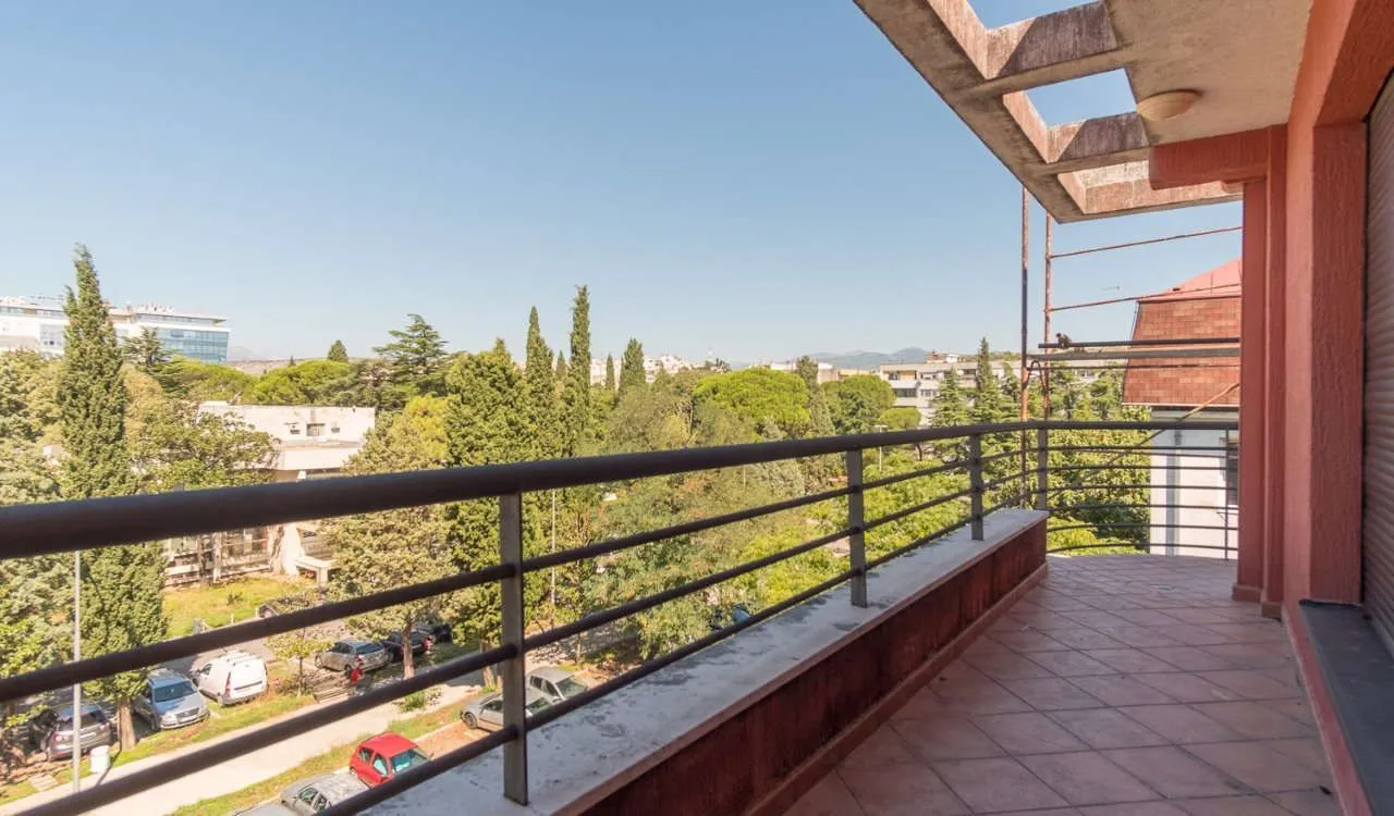 Prostrani popločani balkon sa pogledom na zelenilo i okolne zgrade.
