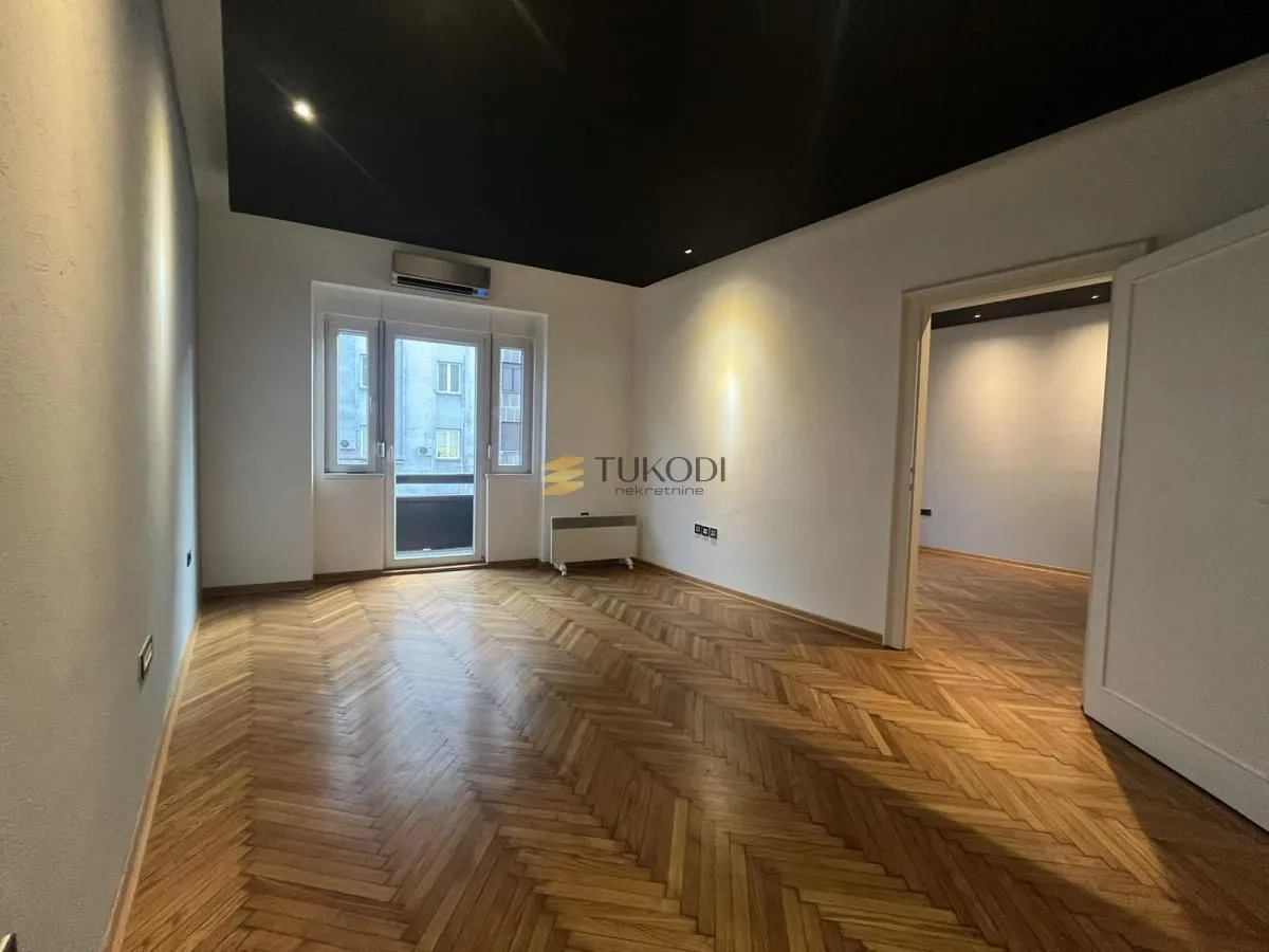 Empty room with hardwood parquet flooring, black ceiling, and access to a balcony.