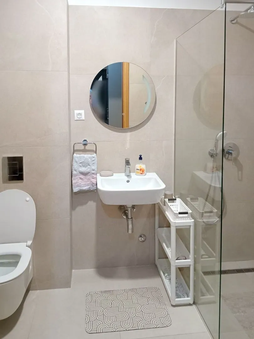 Modern bathroom with a walk-in shower, washbasin, and round mirror.