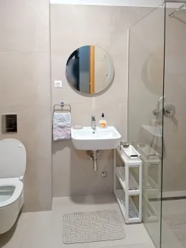 Modern bathroom with a walk-in shower, washbasin, and round mirror. - image 5