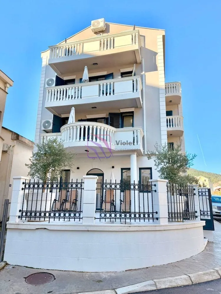 Front view of a multi-story residential building with balconies and a fenced yard.
