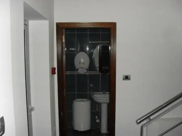 View of a small bathroom with dark tiles and a sink through an open doorway.