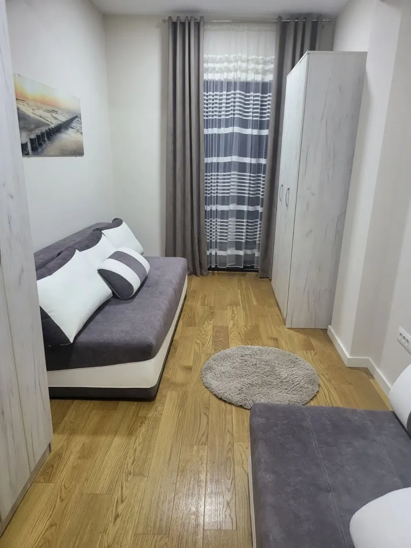 Bright and simple living room with a sofa, wardrobe, and wooden flooring.