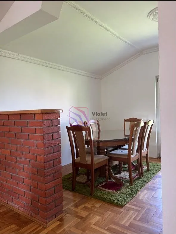 Dining area with a wooden table and chairs, parquet flooring, and a low brick wall.