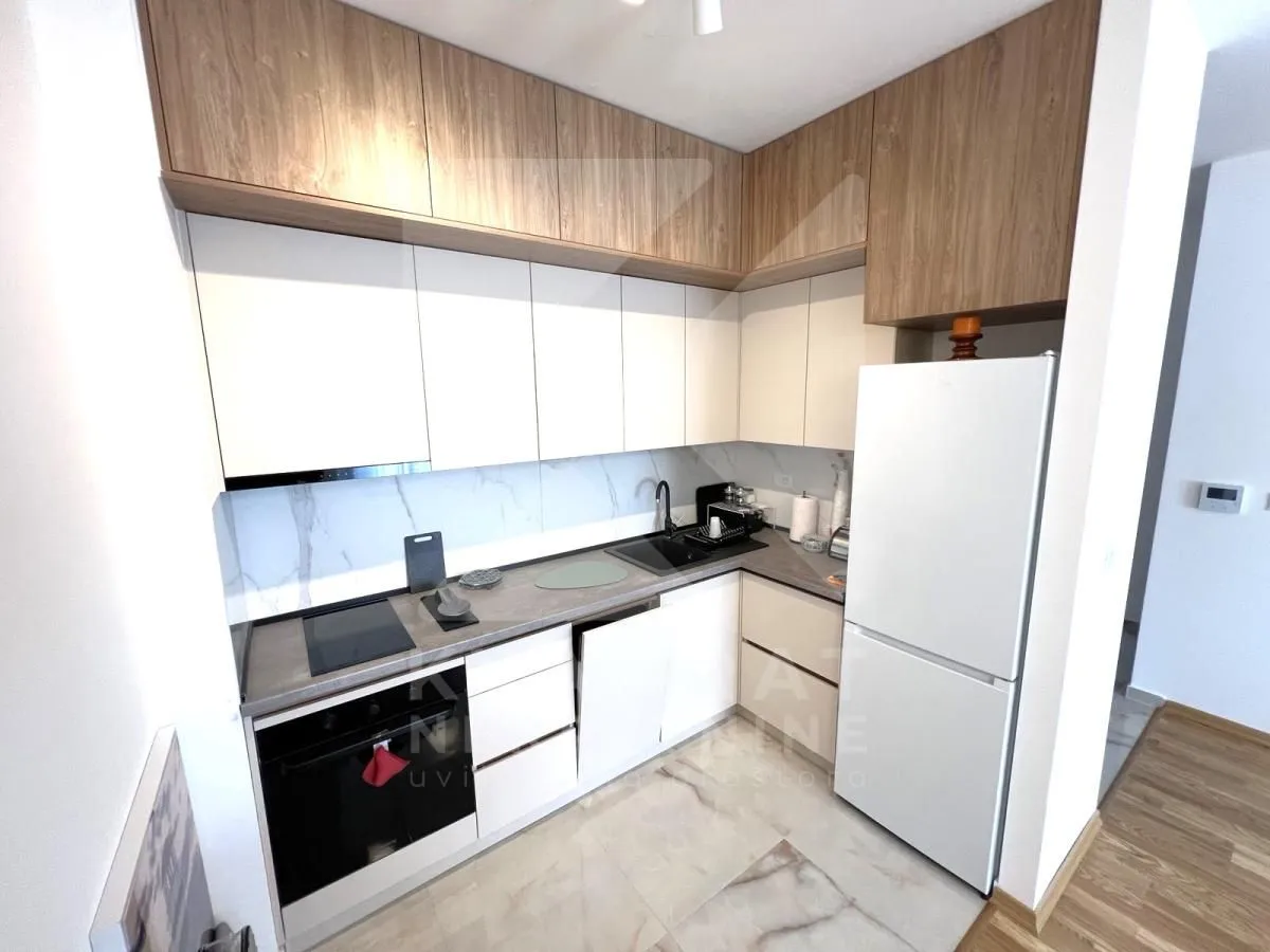 Modern kitchen with white units, wooden upper cabinets, and built-in appliances.