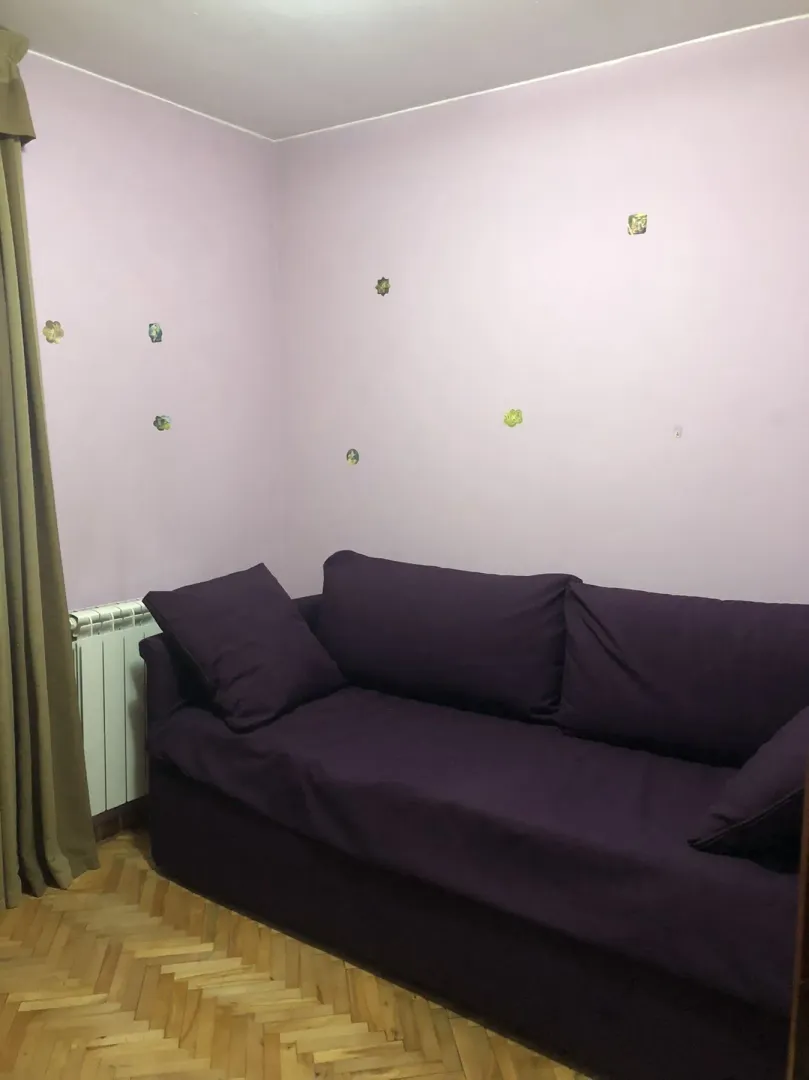 A room with a purple sofa, parquet flooring, and light-colored walls.