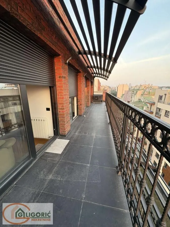 Prostrani popločani balkon sa metalnom ogradom i pogledom na grad.