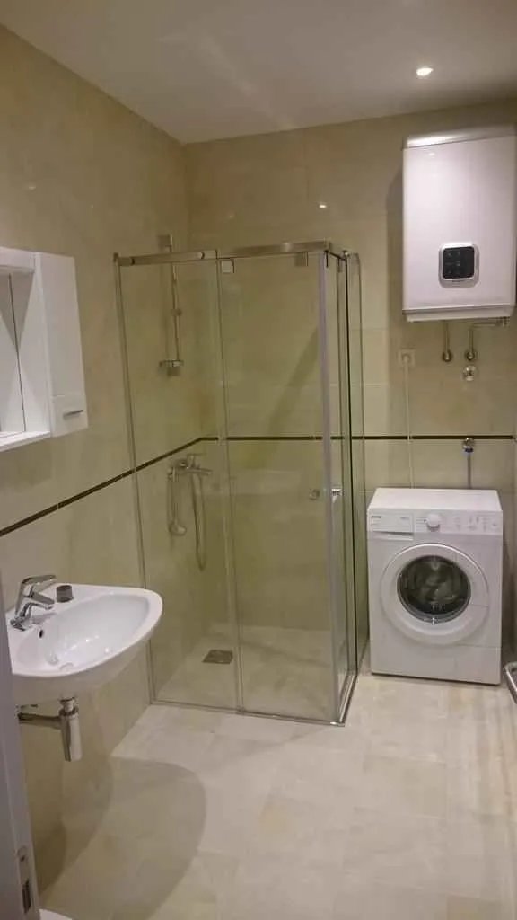 Svijetlo kupatilo sa tuš kabinom, umivaonikom i veš mašinom.