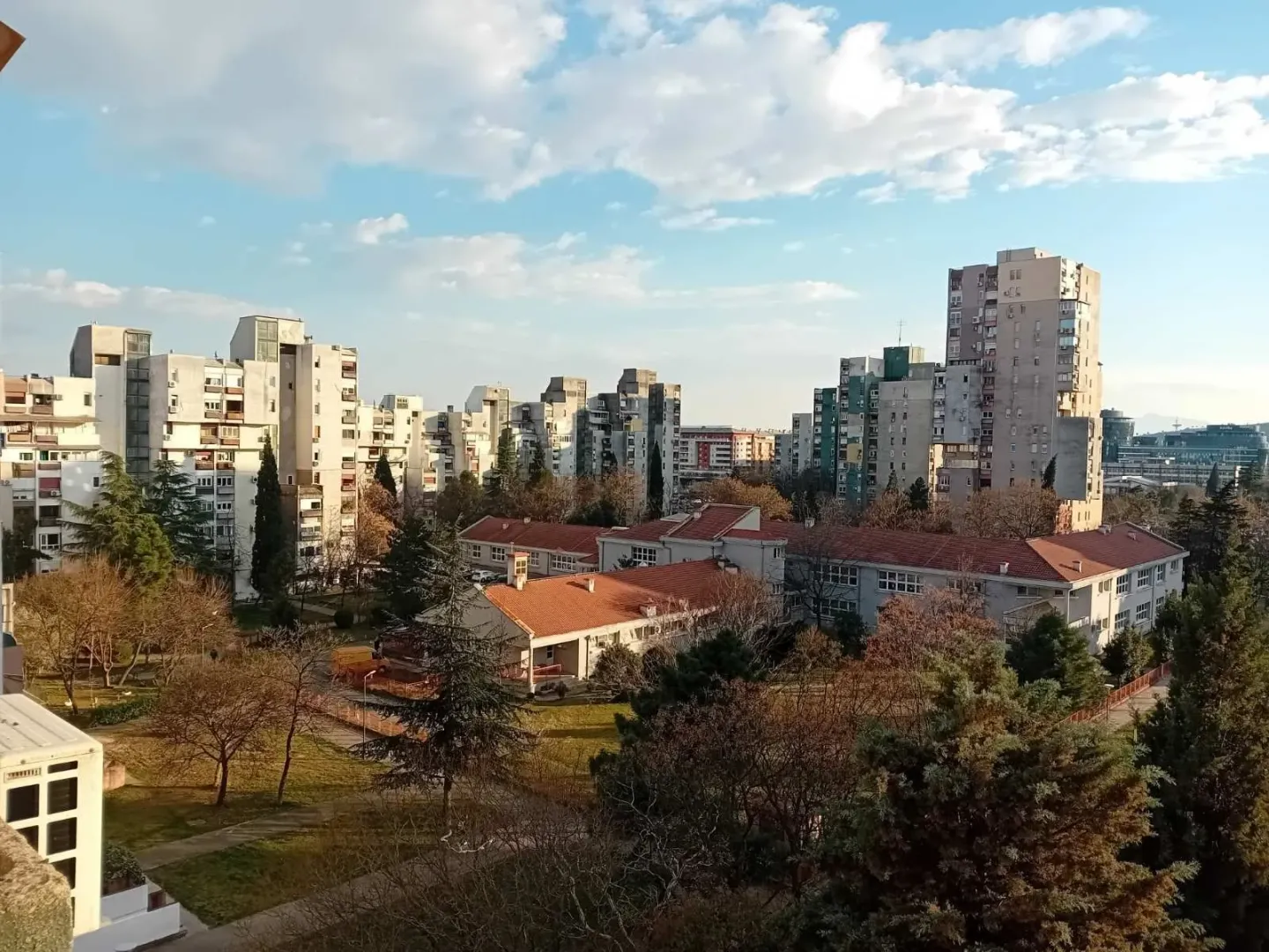 Pogled sa prozora ili terase na stambeni kvart sa drvećem i višespratnicama.