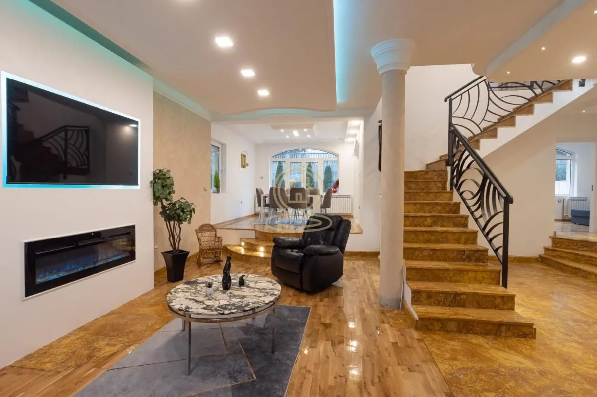 Spacious living room with a fireplace, TV, interior staircase, and dining area in the background.
