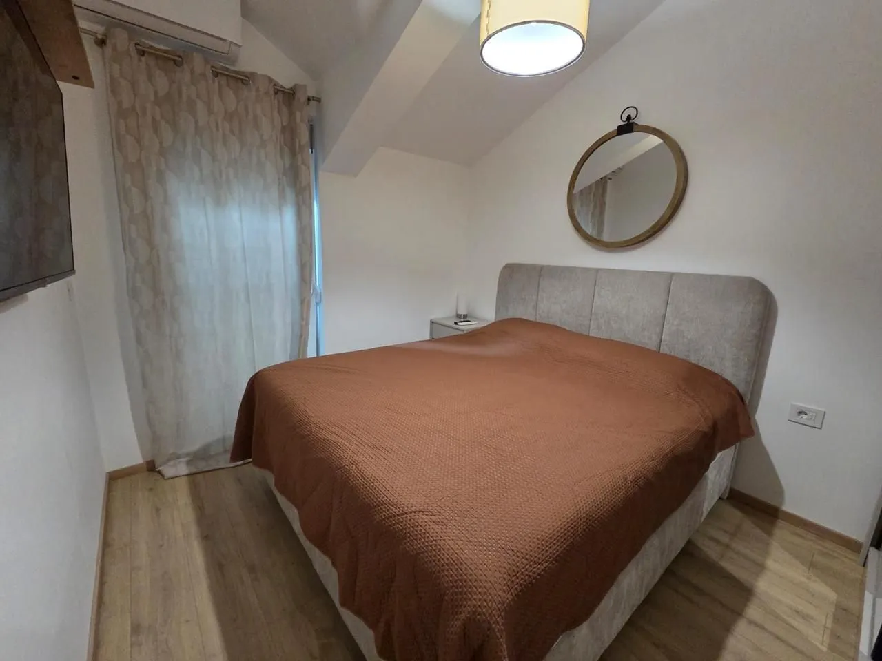Bedroom with a double bed, a wall mirror, and a window with a curtain.