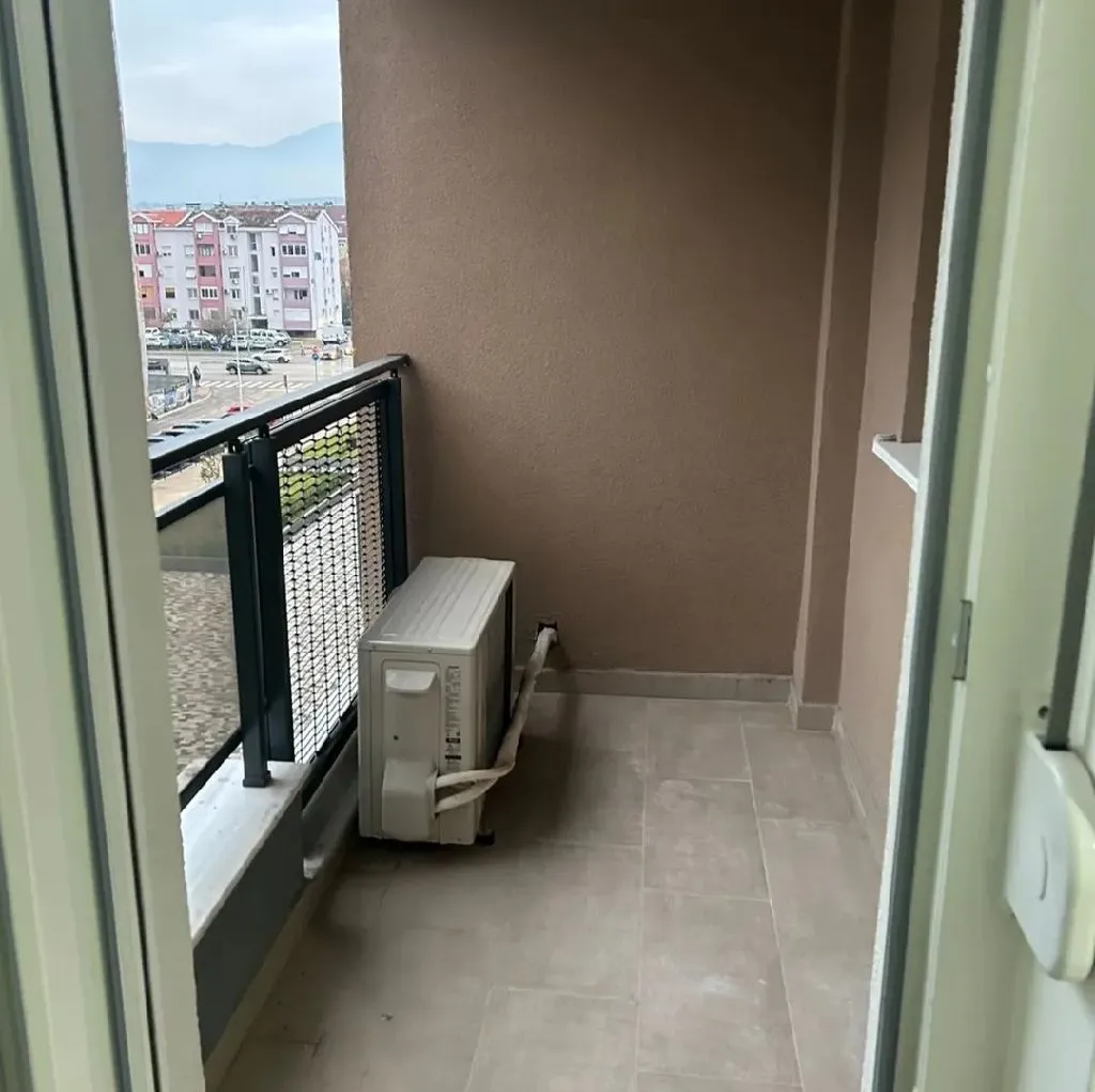 Manji popločani balkon sa spoljnom jedinicom klima uređaja i ogradom.