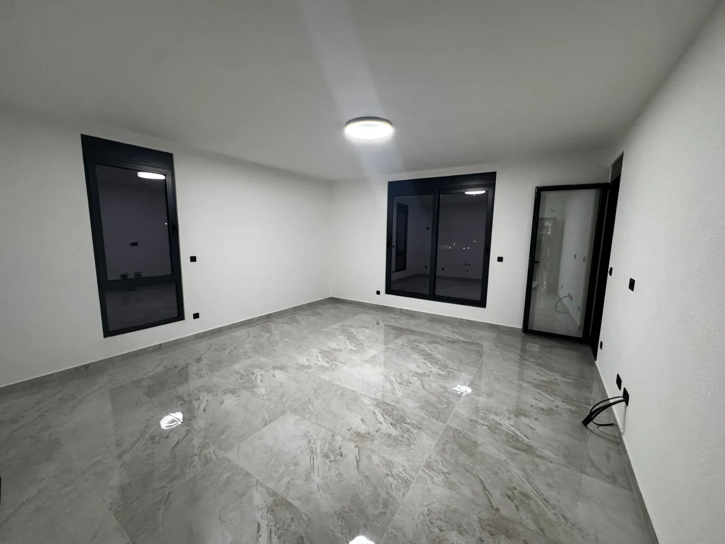 Empty room with ceramic tiles and black window frames.