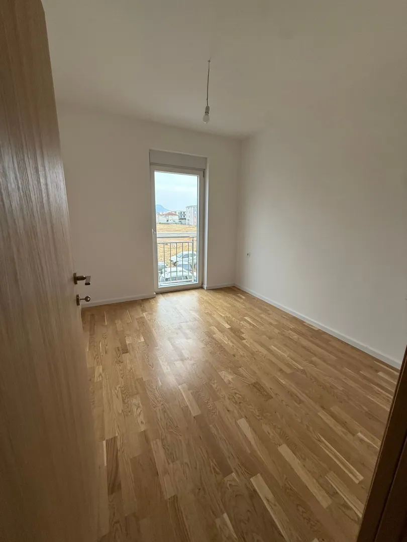 Prazna soba sa parketom i balkonskim vratima.