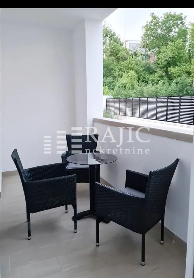 Small covered terrace furnished with a black wicker table and chairs overlooking greenery.