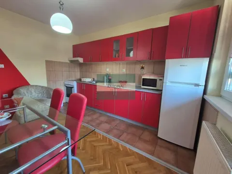 Kuhinja sa crvenim elementima, trpezarijskim stolom i belim frižiderom. - image 3