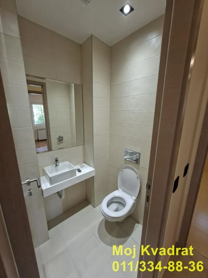 Manje kupatilo sa WC šoljom, umivaonikom i ogledalom.