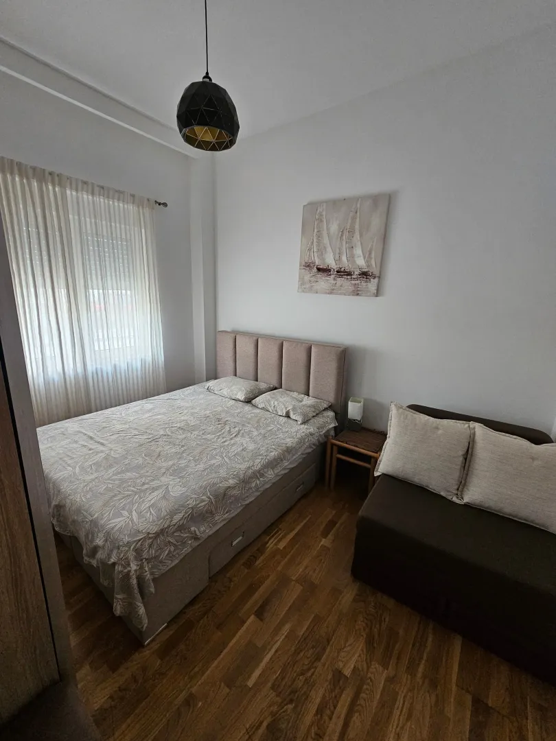 Furnished bedroom with a double bed, sofa, and a window with curtains.