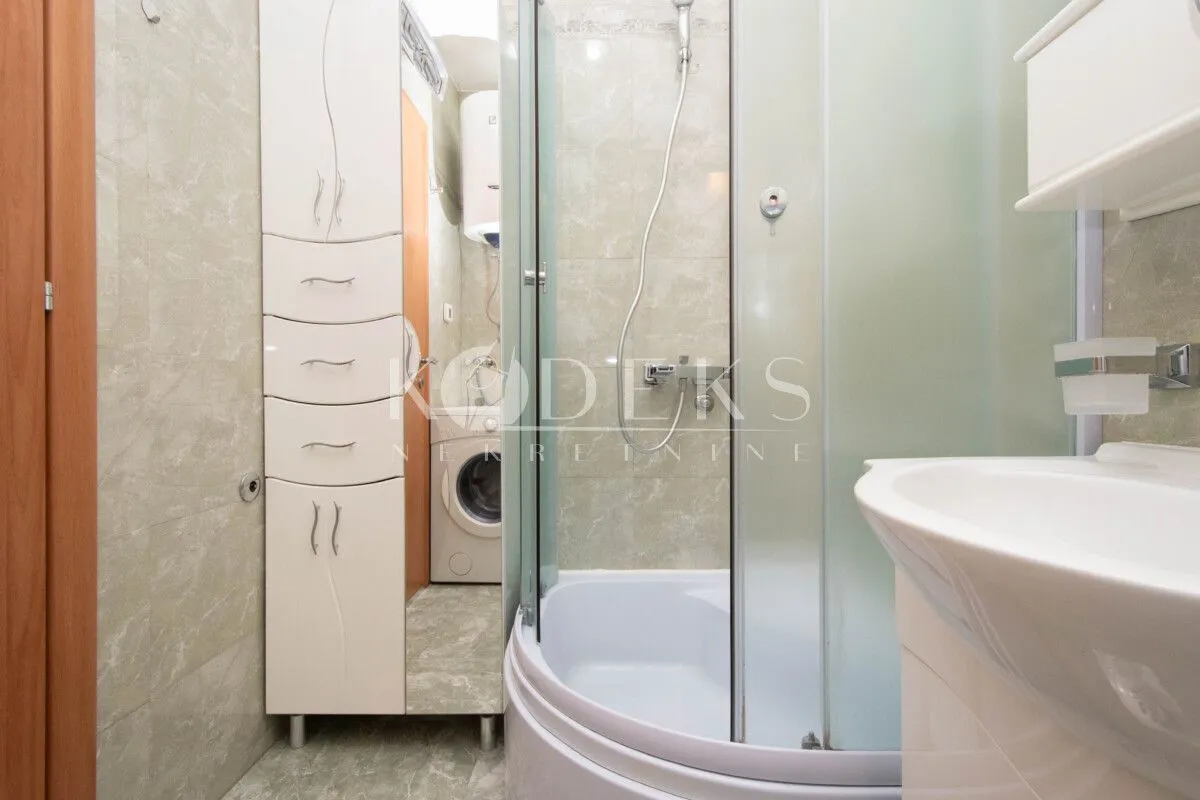Bathroom with a shower cabin, washbasin, cabinet, and washing machine.