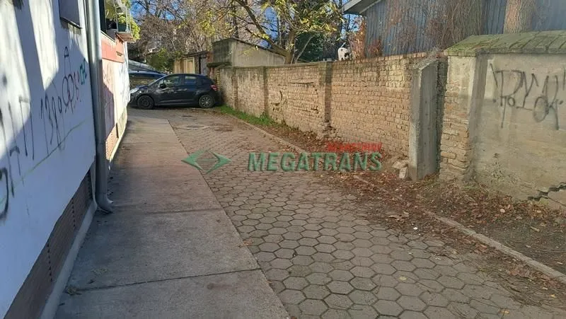 Pogled na popločano dvorište sa parkiranim automobilom pored zgrade.