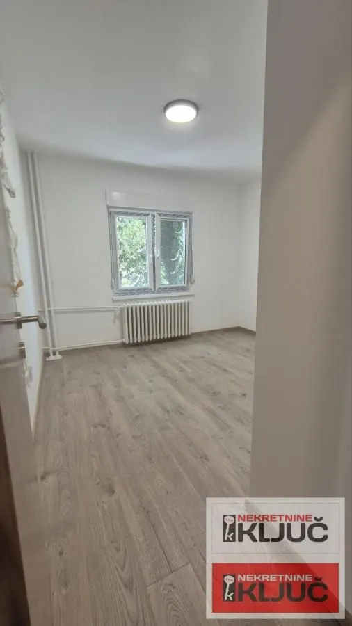 Prazna soba sa laminatom i belim zidovima.