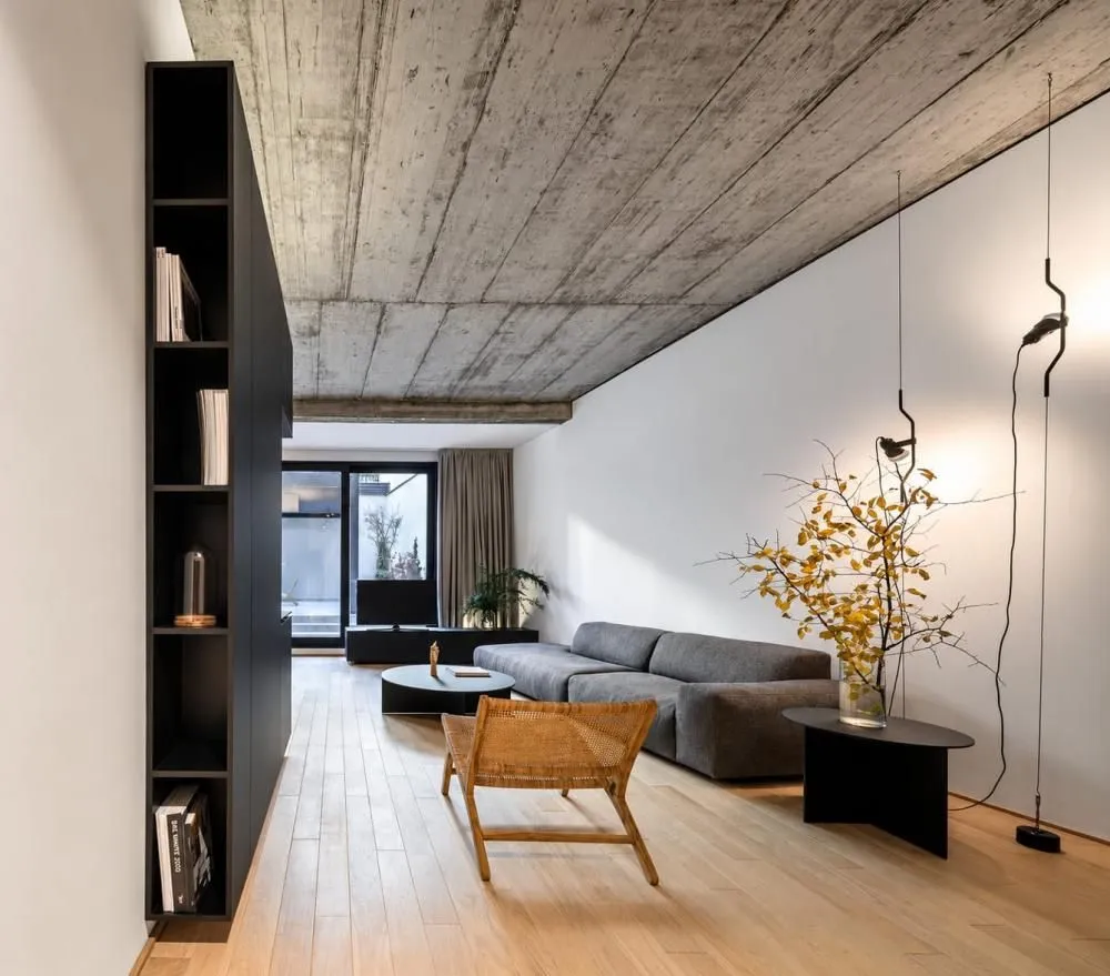 Modern living room with a sofa, shelving unit, and exposed concrete ceiling.