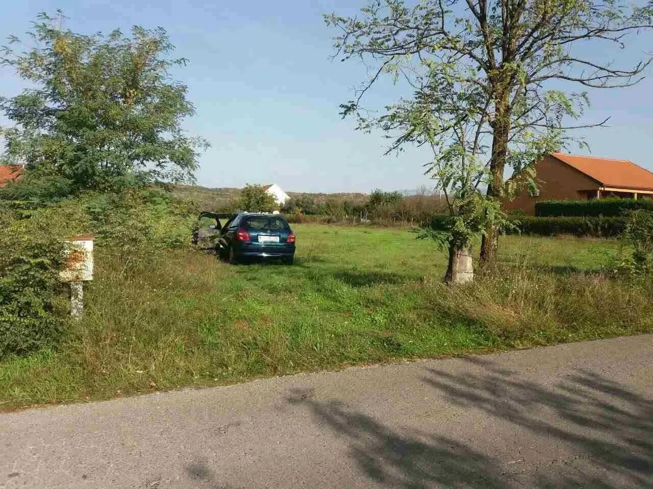 Zeleni plac pored asfaltnog puta sa drvećem.
