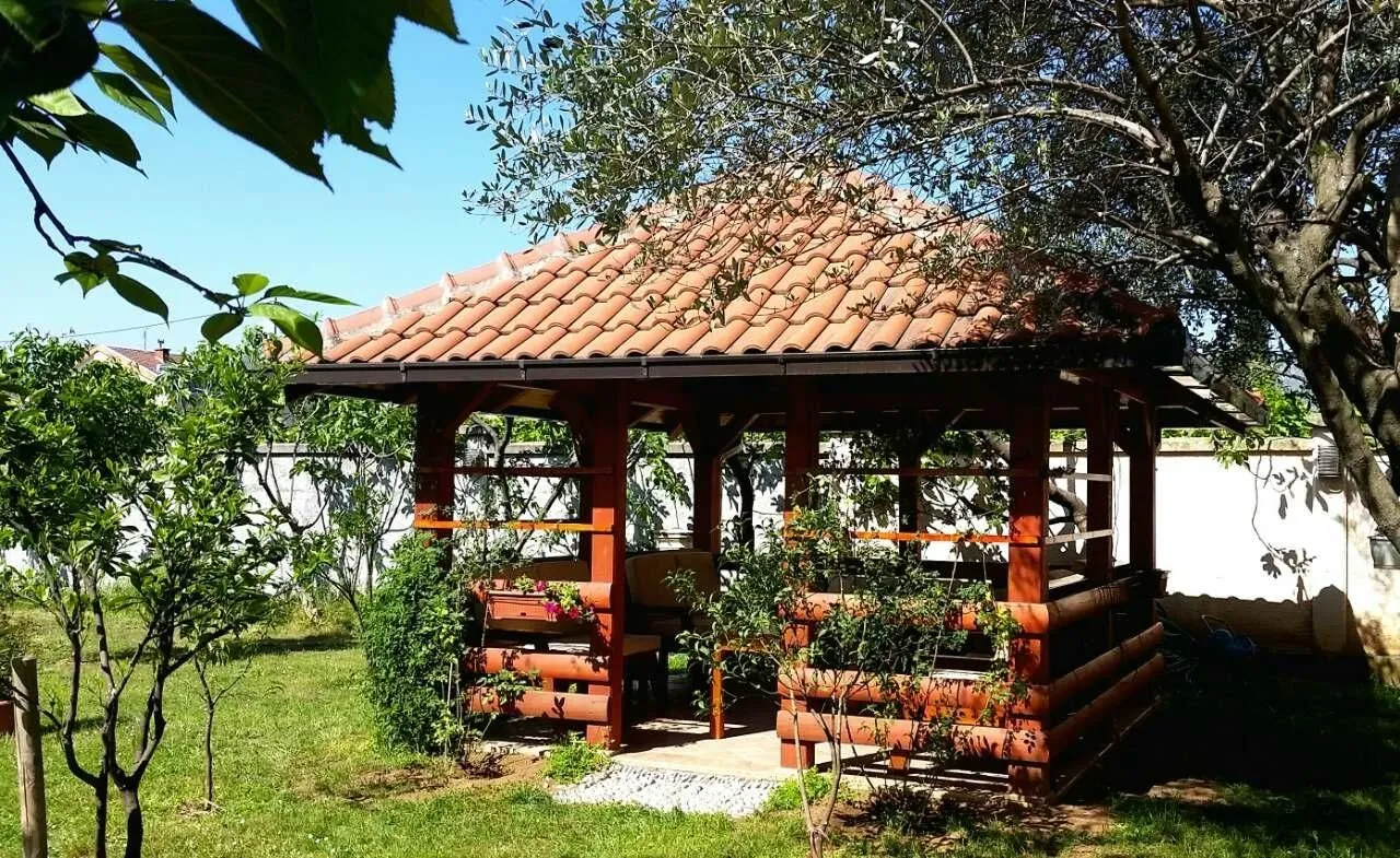 A wooden gazebo surrounded by greenery in the yard.