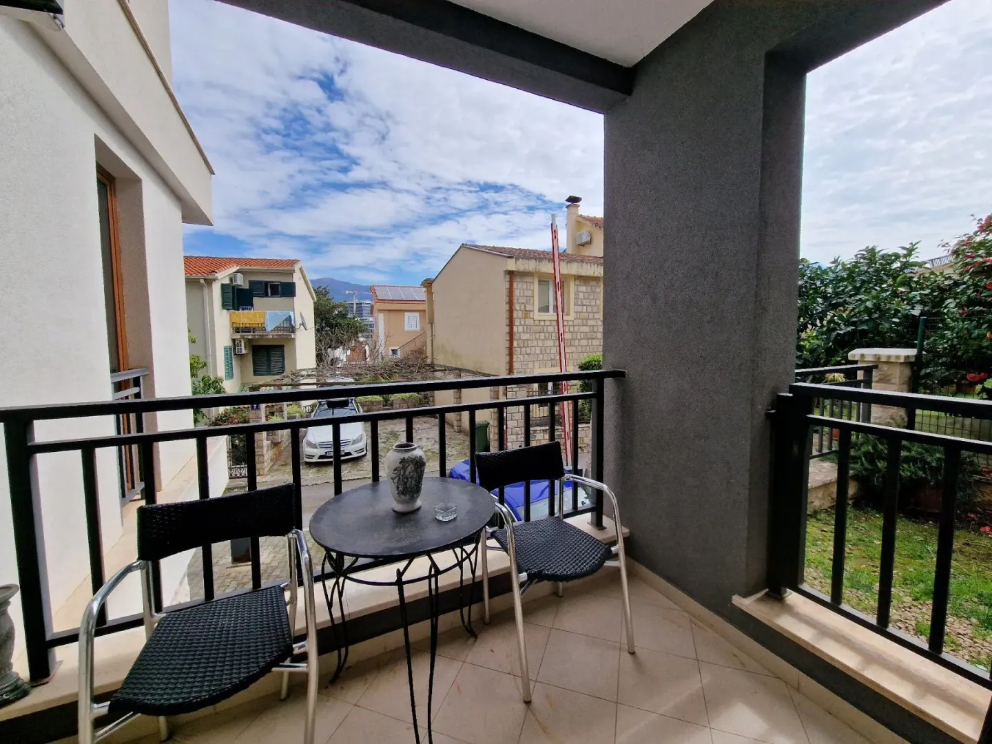 Natkriveni balkon sa garniturom za sjedenje i pogledom na okolne zgrade i dvorište.