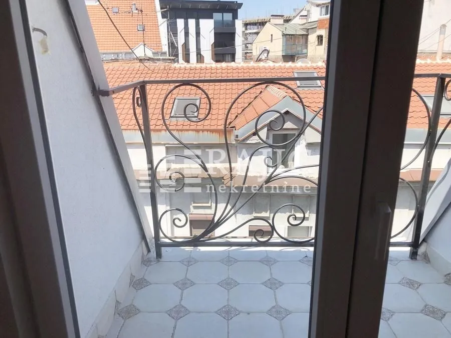 Manji popločani balkon sa ukrasnom metalnom ogradom i pogledom na grad.