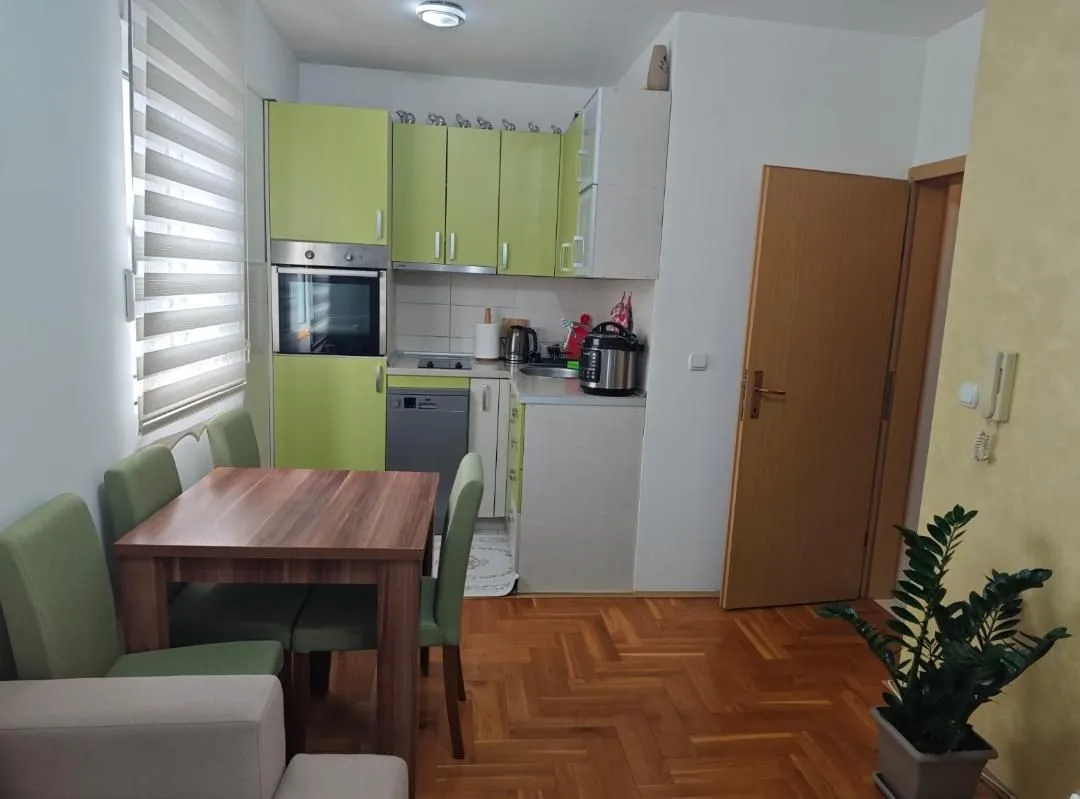 Manja kuhinja sa trpezarijskim stolom i zelenim elementima.