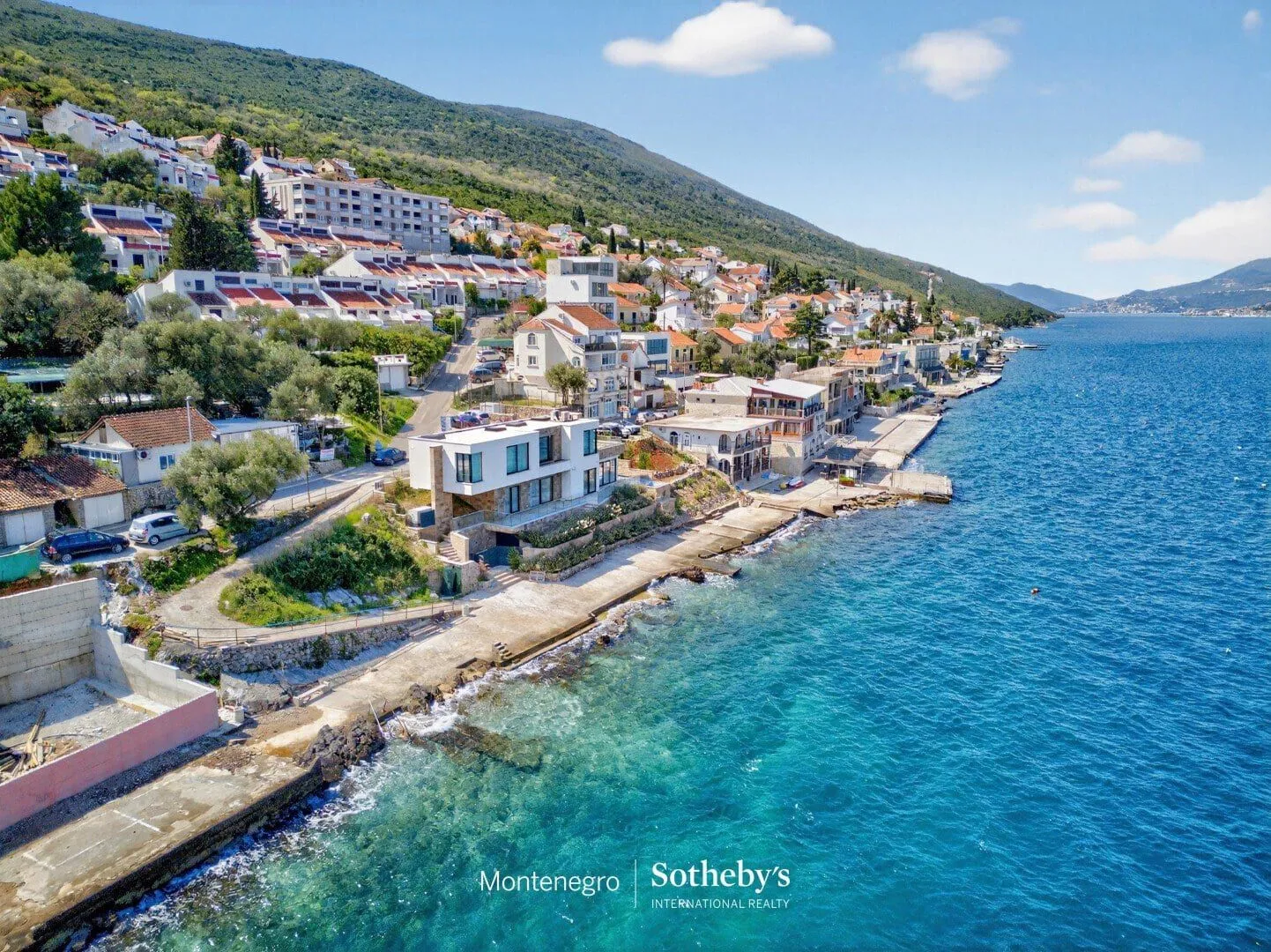 Pogled iz vazduha na obalu i primorsko naselje sa brdom u pozadini.