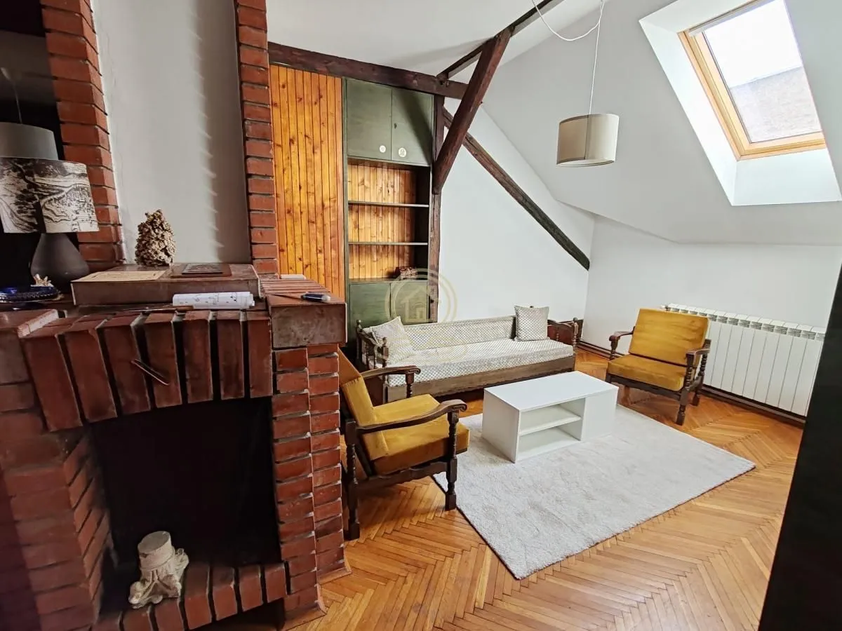 Attic living room with a fireplace, exposed wooden beams and parquet flooring.