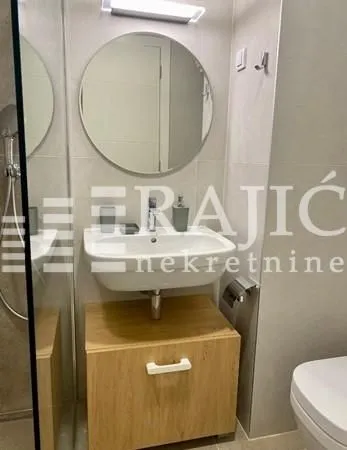 Moderno kupatilo sa umivaonikom, drvenim ormarićem i ogledalom.
