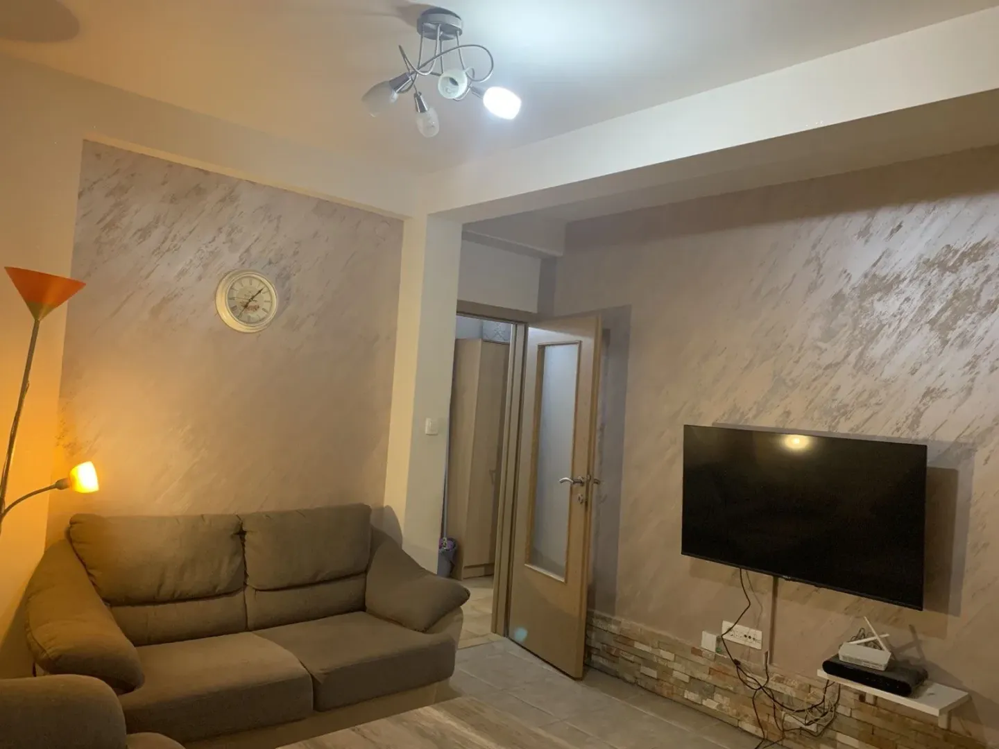 A living room with a comfortable sofa, wall-mounted TV, and decorative lighting.