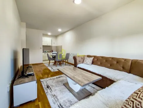 Living room with a sofa, TV, and kitchen in the background. - image 4