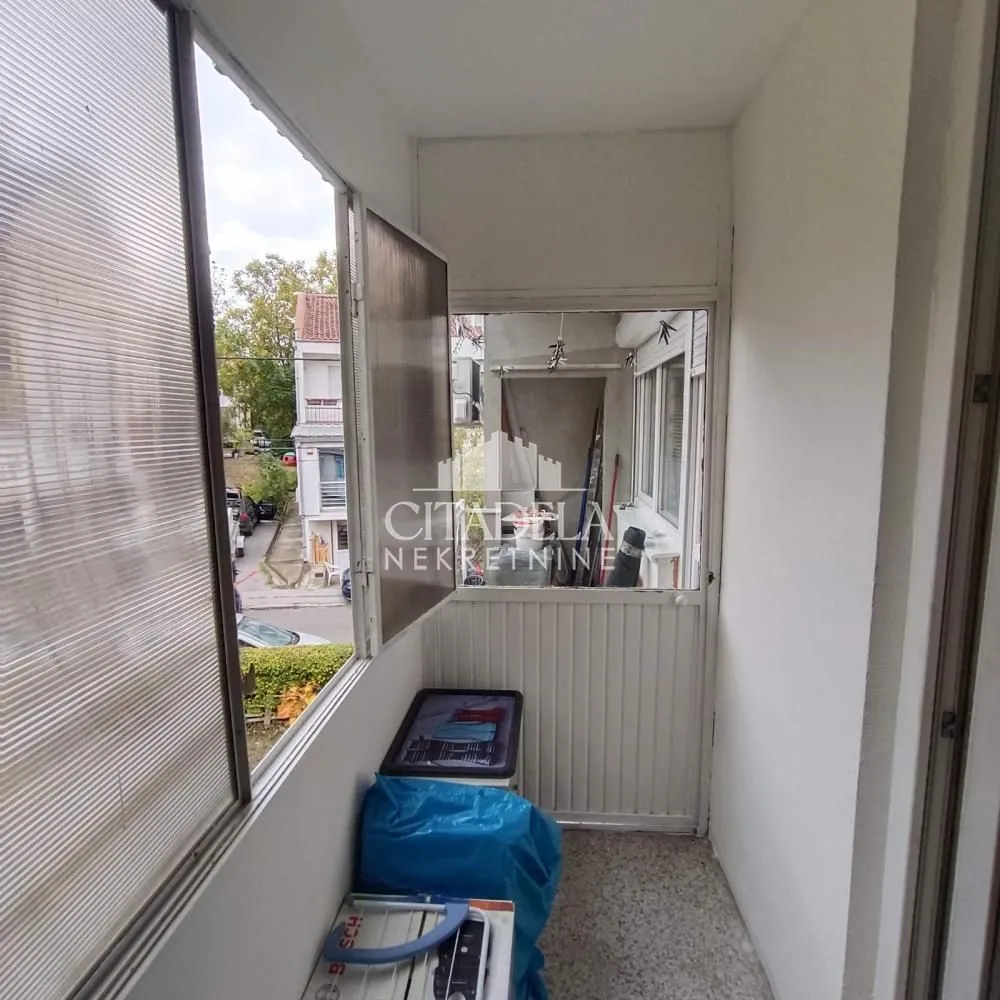 Zastakljeni balkon sa pogledom na ulicu i okolne zgrade.